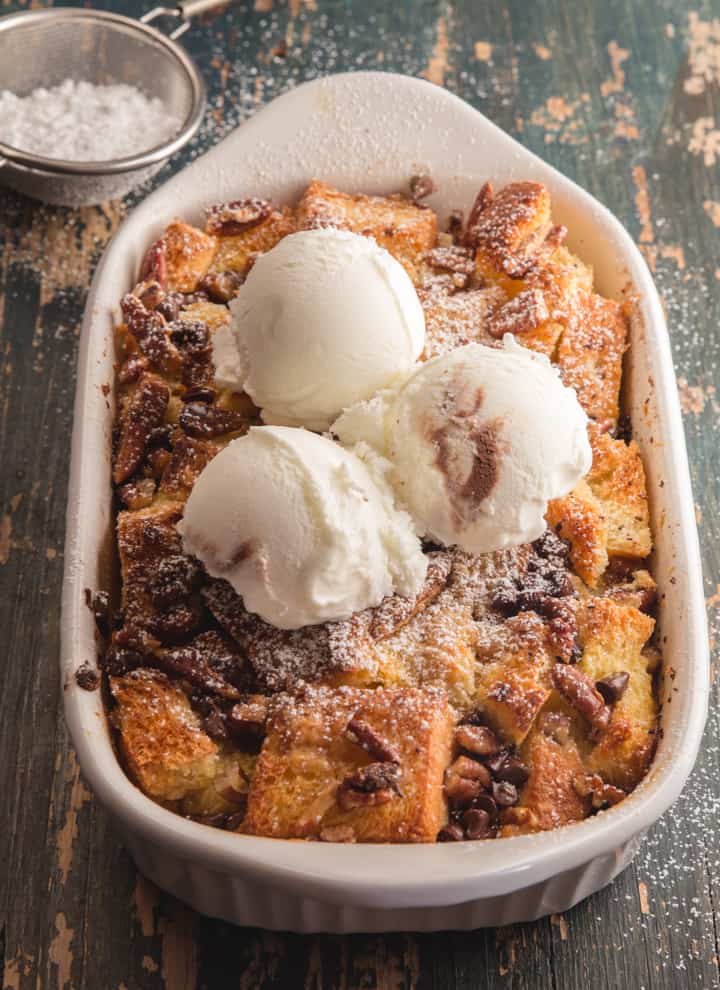 bread pudding in a white pan with 3 scoops of vanilla ice cream on top