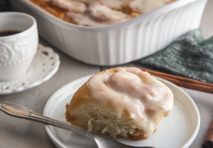 cinnamon rolls in a pan and one on a white plate with a fork