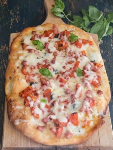 pizza with tomatoes, pancetta & cheese on a wooden board