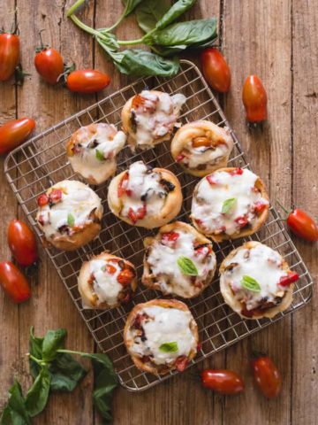 pizza muffins on a wire rack with fresh basil and tomatoes around it