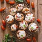 pizza muffins on a wire rack with fresh basil and tomatoes around it