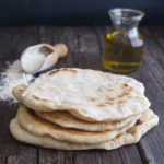 4 flatbreads on top of each other with flour and oil in the back ground
