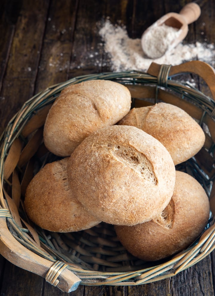 whole wheat buns in a basket with a small scoop of flour